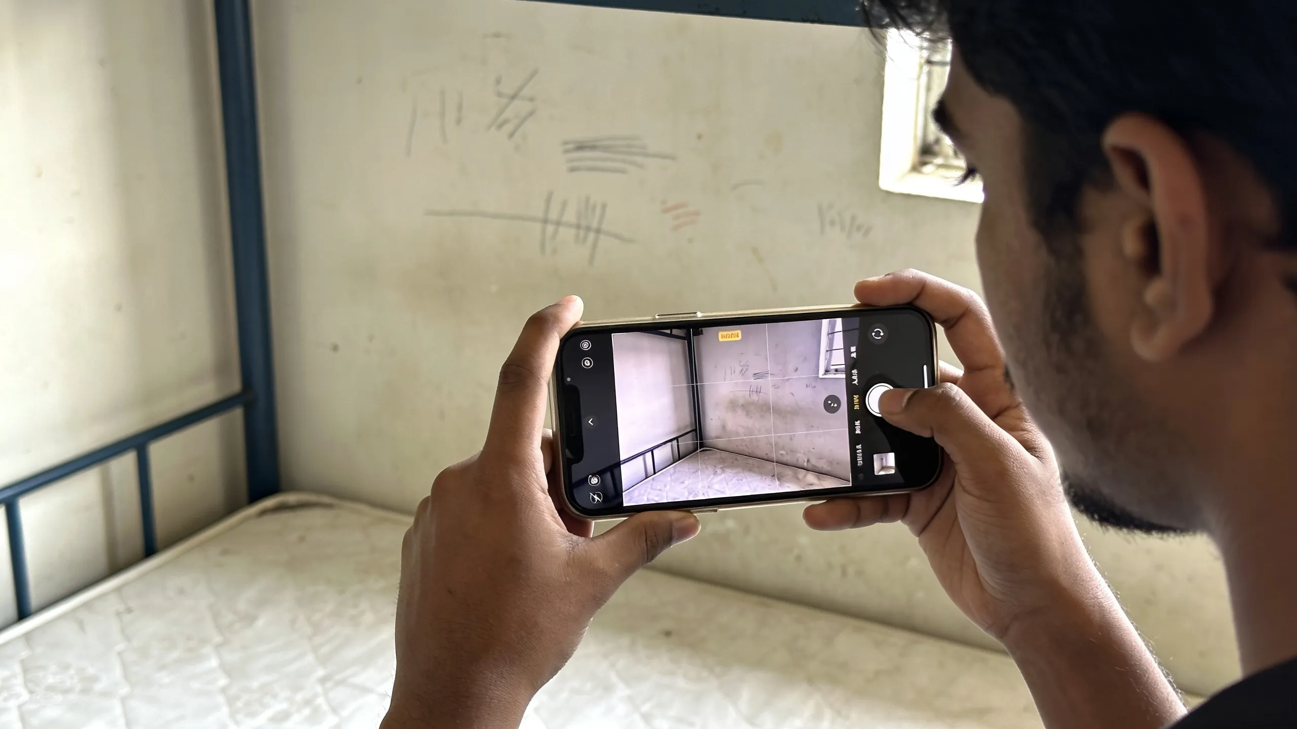 Student documenting hostel room condition on phone camera before checkout